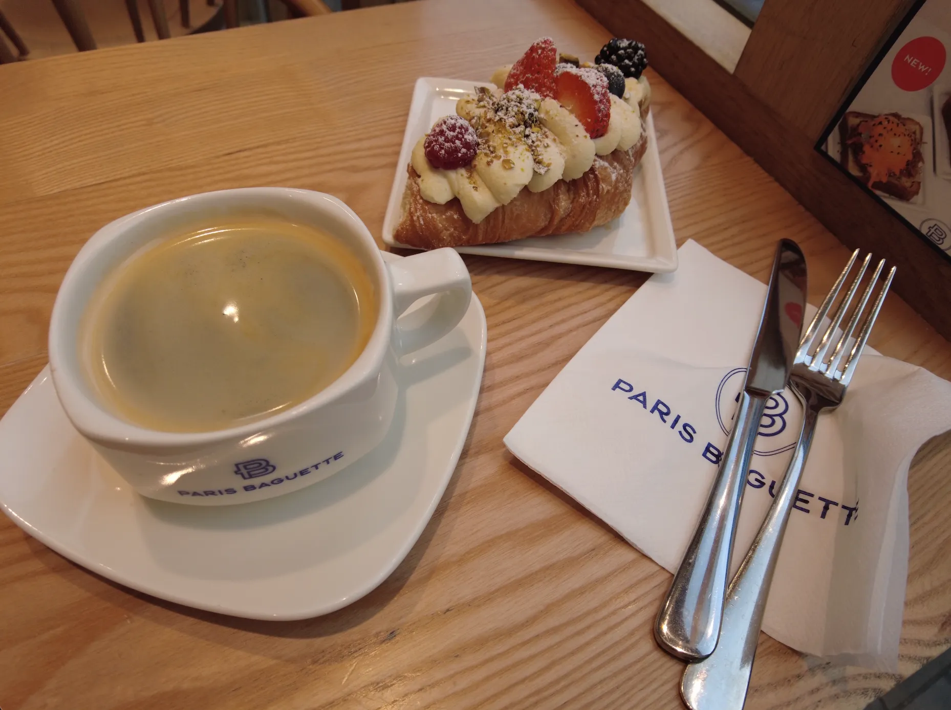 A photo of a cup of coffee and a very fancy croissant covered in fruits.