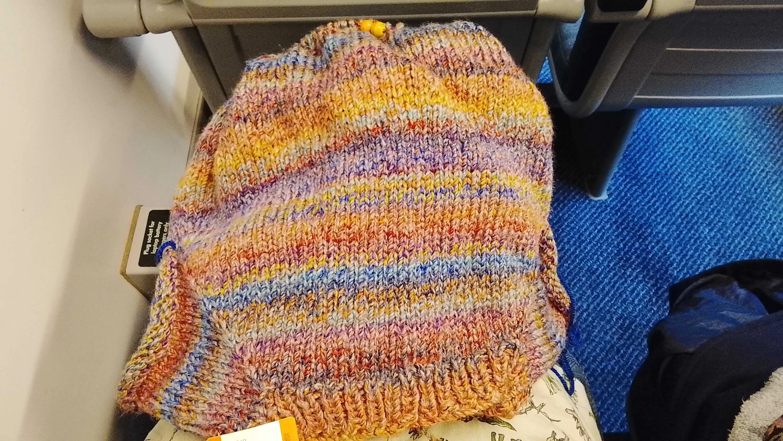An overhead photo of an in-progress jumper on my lap, it's about navel length with no arms.